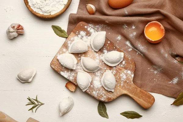 Board with raw dumplings on white wooden background — Stock Photo, Image