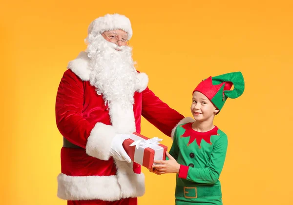 Santa Claus and little elf kid with gift on color background — Stock Photo, Image