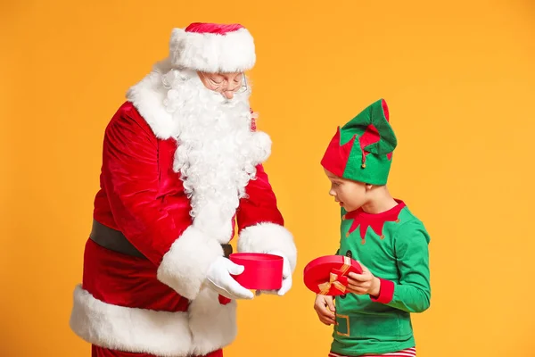 Weihnachtsmann und kleine Elfenkind Eröffnungsgeschenk auf farbigem Hintergrund — Stockfoto