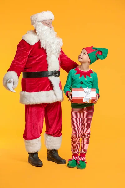 Santa Claus and little elf kid with gift on color background — ストック写真
