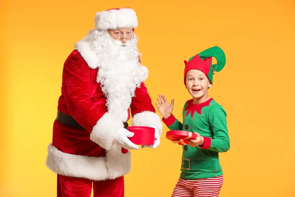 Santa Claus y pequeño niño elfo abriendo regalo sobre fondo de color —  Fotos de Stock