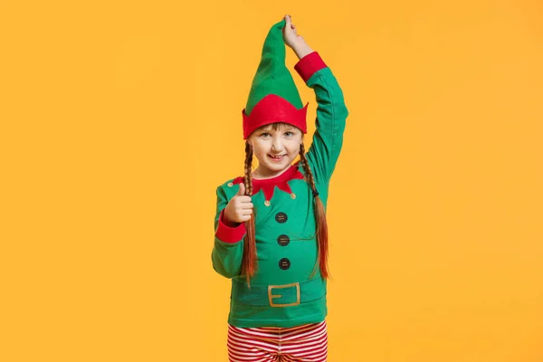 Menina no traje de elfo mostrando gesto de polegar para cima no fundo de cor — Fotografia de Stock
