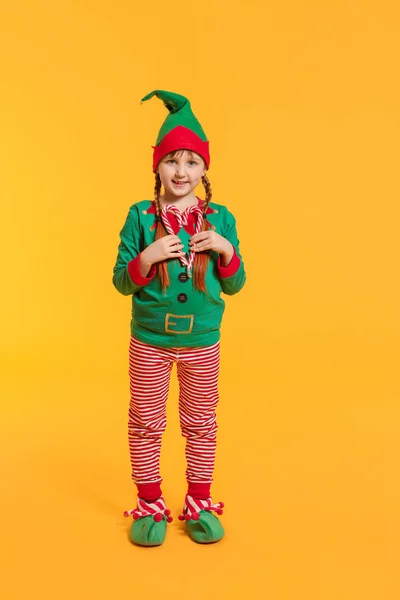 Liten flicka i kostym nisse och med godis käppar på färg bakgrund — Stockfoto