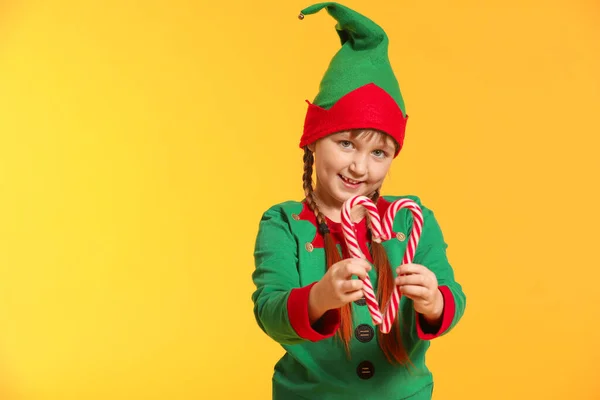 Little girl in costume of elf and with candy canes on color background — Stock Photo, Image
