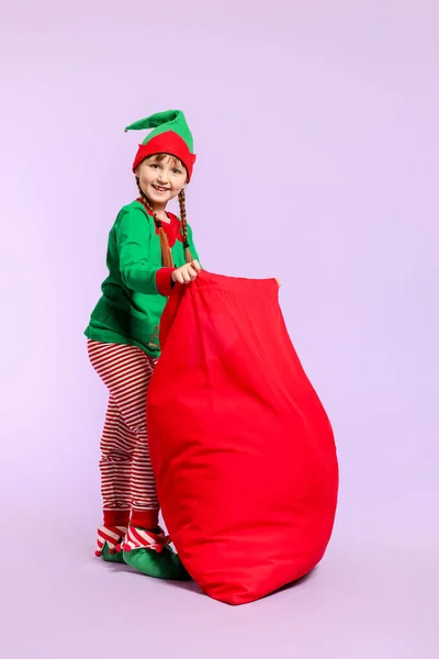 Bambina in costume da elfo e con grande borsa di Babbo Natale su sfondo di colore — Foto Stock