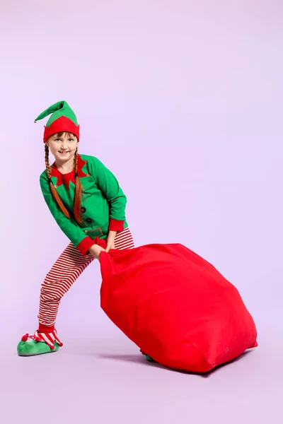 Little girl in costume of elf and with big Santa Claus bag on color background — Stock Photo, Image