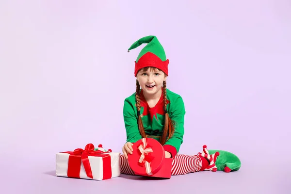 Little girl in costume of elf opening gift on color background — Stock Photo, Image