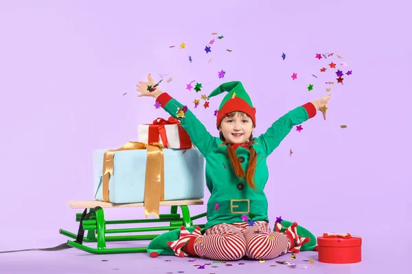 Kleines Mädchen im Elfenkostüm, mit Geschenken und Schlitten, die Konfetti auf farbigem Hintergrund werfen — Stockfoto