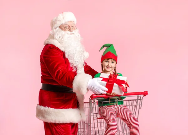 Mikulás és kis manó gyerek ajándék ül bevásárlókosár színes háttér — Stock Fotó