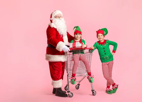 Weihnachtsmann und kleine Wichtelkinder mit Geschenk und Warenkorb auf farbigem Hintergrund — Stockfoto