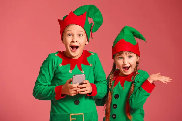 Crianças surpresas no traje de elfo e com telefone celular no fundo de cor — Fotografia de Stock