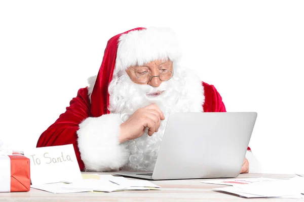 Kerstman met laptop aan tafel op witte achtergrond — Stockfoto