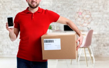 Ofisinde kutu ve cep telefonu olan yakışıklı teslimatçı.