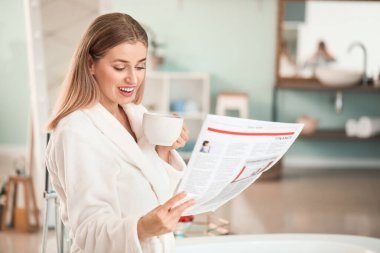 Genç ve güzel bir kadın banyoda çay içip gazete okuyor.