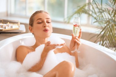 Güzel genç bayan banyoda şampanya içiyor.
