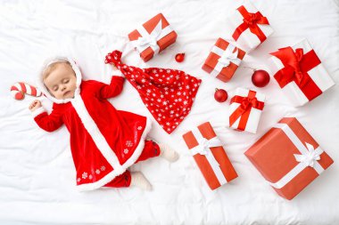 Noel Baba kostümü içinde küçük şirin bir bebek ve yatağında hediyeler var.