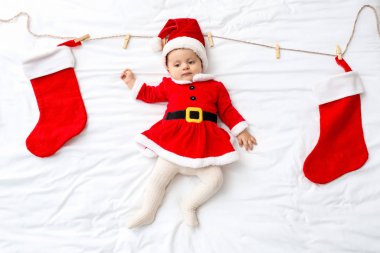 Noel Baba kostümlü şirin bir bebek ve Noel çorapları yatakta yatıyor.