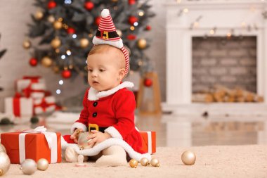 Noel Baba kostümlü şirin bir bebek ve evde Noel hediyeleri var.