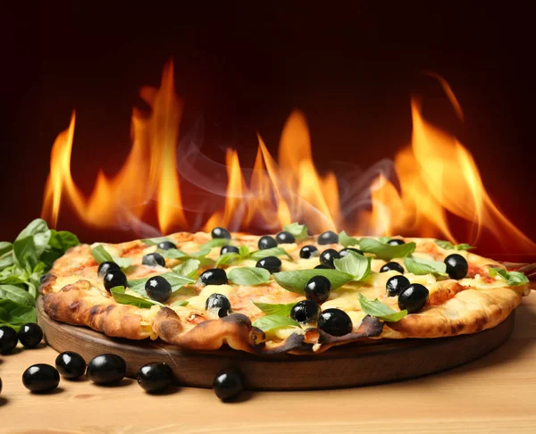 Varm pizza med brinnande låga på bordet mot mörk bakgrund — Stockfoto