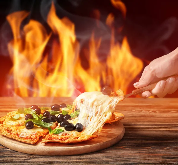 Frau nimmt Stück heiße Pizza mit Oliven vom Tisch gegen brennende Flamme — Stockfoto