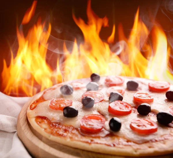 Hot pizza med brinnande låga ombord mot färg bakgrund — Stockfoto