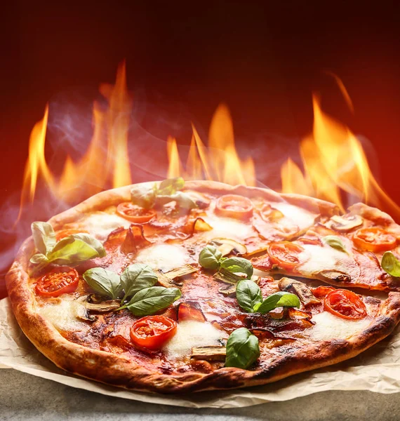 Heiße Pizza mit brennender Flamme auf Tisch vor farbigem Hintergrund — Stockfoto