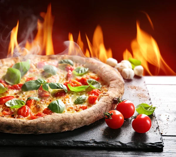 Heiße Pizza mit brennender Flamme auf Tisch vor farbigem Hintergrund — Stockfoto