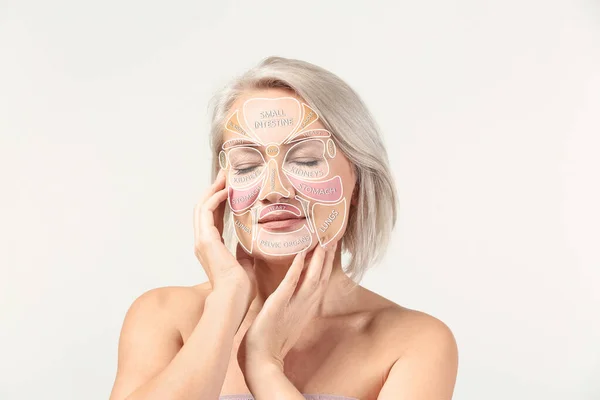 Mujer madura con carta de masaje reflexología en su cara contra fondo claro —  Fotos de Stock