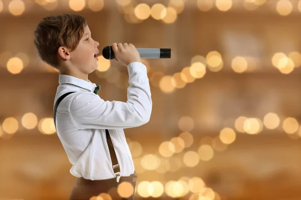 Menino bonito com microfone cantando contra luzes embaçadas — Fotografia de Stock