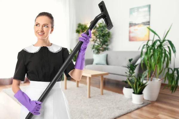 Portrait of beautiful female housekeeper with vacuum cleaner in living room — ストック写真