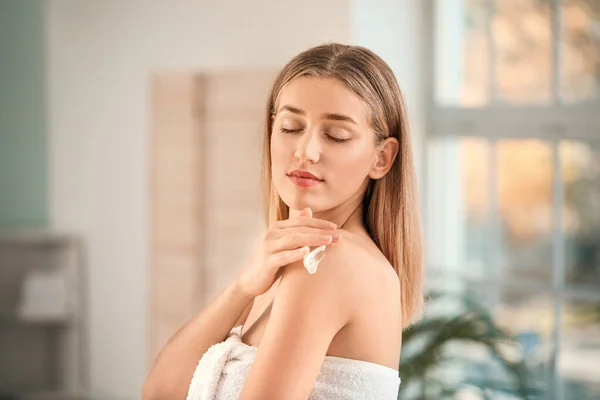 Beautiful young woman applying cream on her shoulder in bathroom — Stock Photo, Image