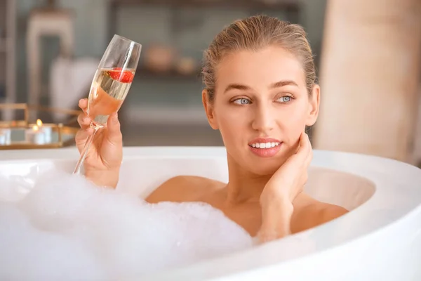 Schöne junge Frau trinkt Champagner im Badezimmer — Stockfoto