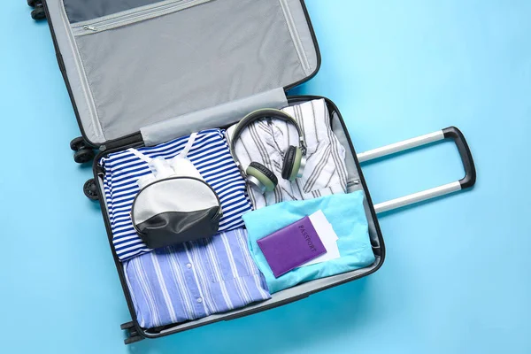 Suitcase with packed clothes, passport and accessories on color background