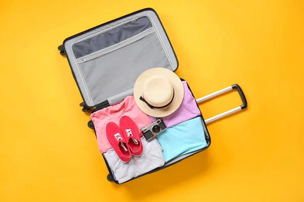 Suitcase with packed clothes and photo camera on color background