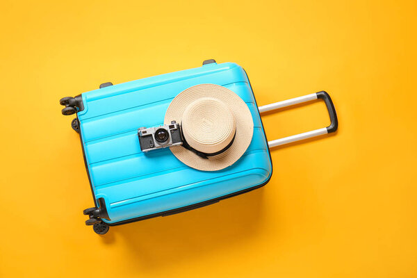 Suitcase with hat and photo camera on color background