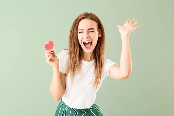 Beautiful happy young woman with small red heart on color background — Stock Photo, Image