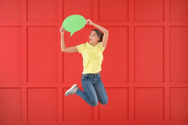 Jumping young woman with speech bubble against color background — Stock Photo, Image