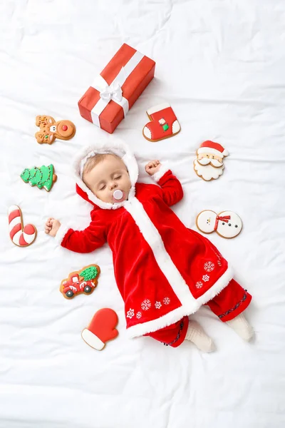 Mignon petit bébé en costume de Père Noël, avec biscuits et cadeau couché sur le lit, vue sur le dessus — Photo