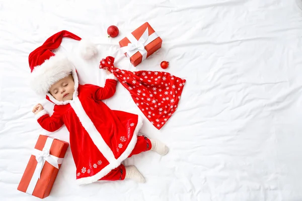 Bebê bonito em traje de Papai Noel e com presentes deitados na cama, vista superior — Fotografia de Stock