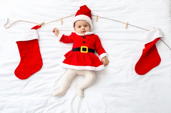 Bebê bonito em traje de Papai Noel e com meias de Natal deitado na cama, vista superior — Fotografia de Stock