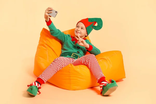 Little boy in costume of elf taking selfie on color background — Stock Photo, Image