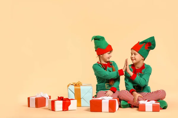 Little children in costume of elf and with gift giving high-five to each other on color background — Stock Photo, Image