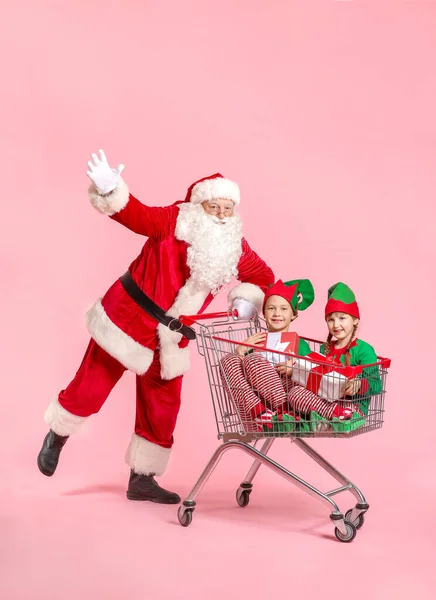 Mikulás és a kis manó gyerekek ajándékok ül bevásárlókosár színes háttér — Stock Fotó