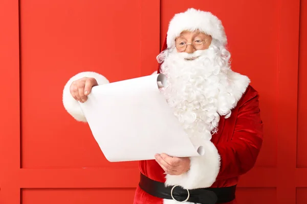 Weihnachtsmann liest Wunschliste auf farbigem Hintergrund — Stockfoto