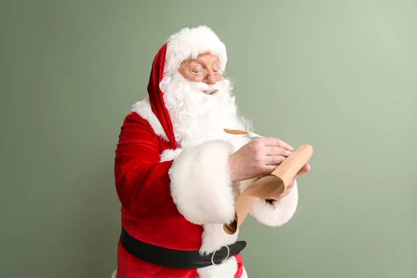 Santa Claus making list of gifts on color background — Stock Photo, Image