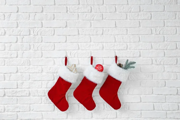 Χριστουγεννιάτικες κάλτσες με δώρα που κρέμονται σε λευκό τοίχο από τούβλα — Φωτογραφία Αρχείου