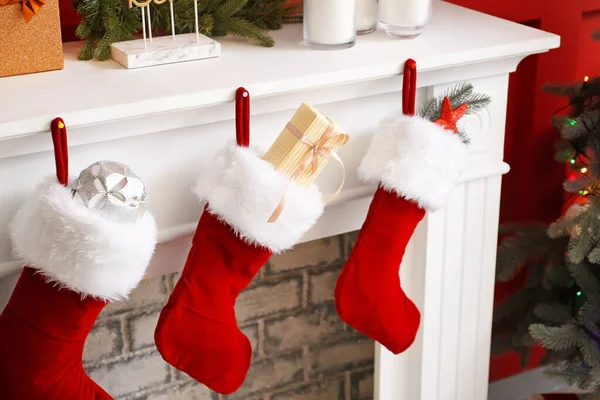 Різдвяні шкарпетки з подарунками, що висять на каміні в кімнаті — стокове фото