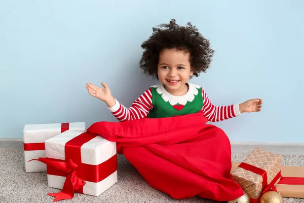 Kleines Mädchen im Elfenkostüm, mit Weihnachtsmann-Tasche und Weihnachtsgeschenken an der Wand — Stockfoto