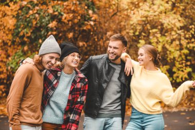 Mutlu genç arkadaşlar birlikte sonbahar parkında dinleniyorlar.