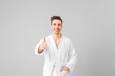 Gri arka planda baş parmak hareketi yapan bornozlu yakışıklı bir adam.